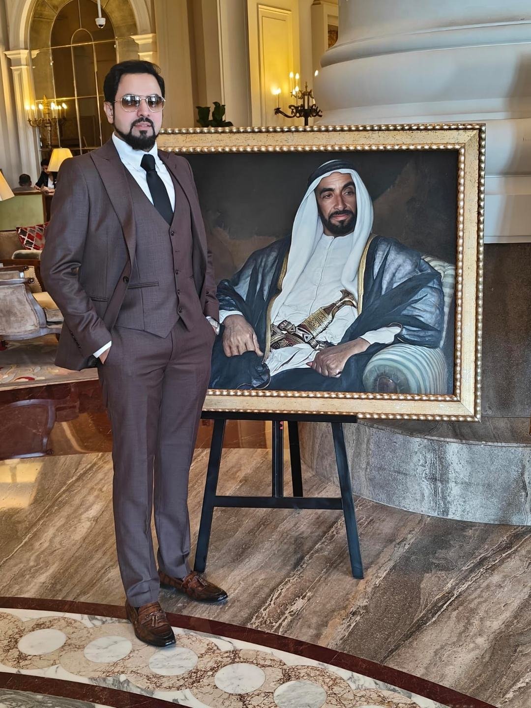 Mohamed Sulthan at a hotel venue, standing beside a large framed portrait.